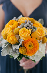 closeup of bridesmaid in purple dress holding a bouquet of orange and yellow roses and ranunculus...