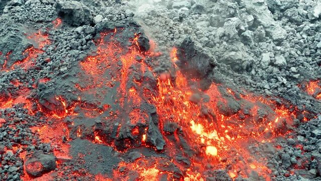 Cinematic steaming red glowing hot lava flow of the Mauna Loa volcano eruption on Hawaii, Big Island in 2022. Shot smartphone camera orange lava and magma flowing down and freezing on black mountain