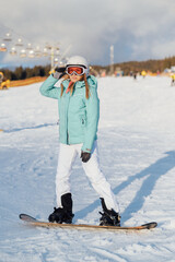 A beautiful girl snowboarder stands on a slope and prepares to descend