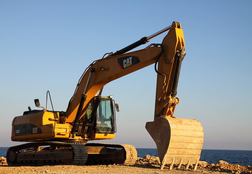 American excavator Caterpillar at sunset. Earthmoving - construction machinery on the seashore.
