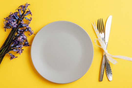 Spring table setting with gray plate and blue hyacinth flowers on yellow background. Top view, flat lay, copy space