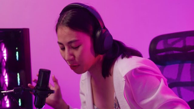 Close-up Young Asia female sit on gaming chair wear headset focus concentration pc screen competition tournament championship in game room at house. Gamer girls raise fist gloats over winning e sport.