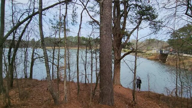 footage along the banks of Lawrenceville Lake with a man fishing surrounded by rippling blue water and bare winter trees at Rhodes Jordan Park in Lawrenceville Georgia USA