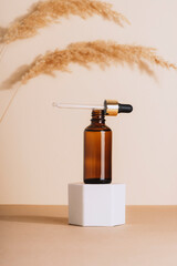 Brown cosmetic serum bottle on a podium and pampas grass on beige background. Natural skin care...