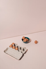 Fresh brown eggs in cardboard box and ceramic bowl on pastel background. Minimal concept.