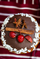 A traditional paska decorated with white and dark Swiss chocolate and cherries, cinnamon and star anise stands on a cherry striped apron. Easter holiday, top view and close up.