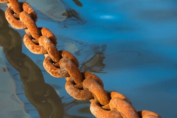 Old rusty chain from the colonial period over blue sea water. Paraty, Brazil. Selective focus. Space for text.