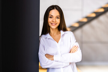 Fototapeta premium Female entrepreneur in her office. Young woman in casuals standing by window and staring at the camera.
