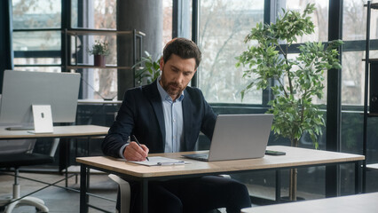 Focused adult businessman work on project in office using laptop writing notes caucasian man...