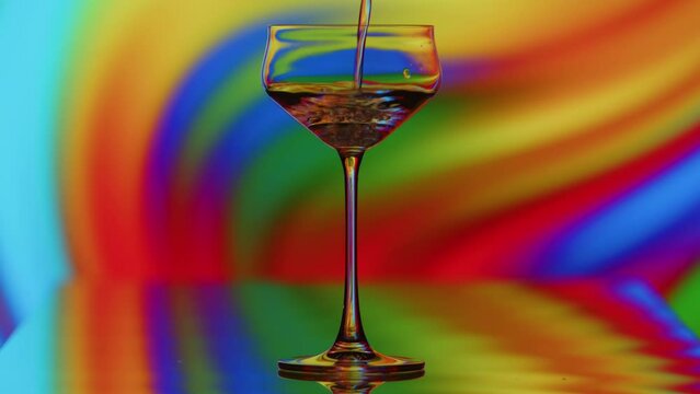 The clear glass is being filled infront of a colorful curvy rainbow background. The reflactions warp with the shape of the glass. High quality 4k footage