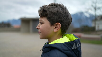 One pensive young boy walking forward outside at park. A contemplative kid wearing winter clothes walks in outdoor city park