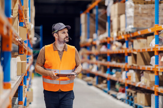 An import and export firm manager is walking trough storage and doing logistic with tablet.