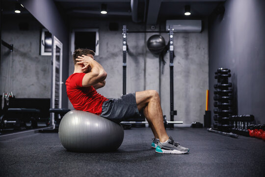 Exercises for the abdomen and whole body, a good balance. A man in excellent shape does sit-ups on a fitness ball indoors at the gym. Personal training and sports motivation. Healthy and strong body