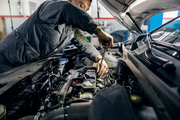 A mechanic is fixing car engine under the hood at mechanic's workshop.