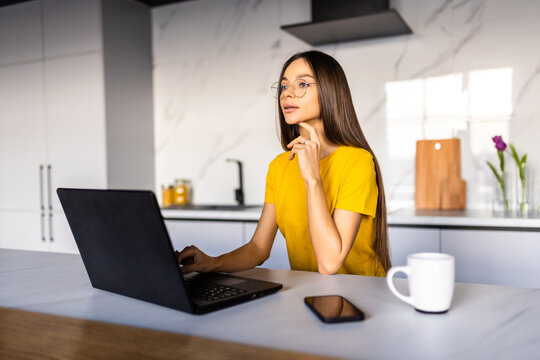 Young Woman In Kitchen Eating Berries And Using Laptop. Happy Woman Looking At Laptop While Standing In Kitchen In Morning.