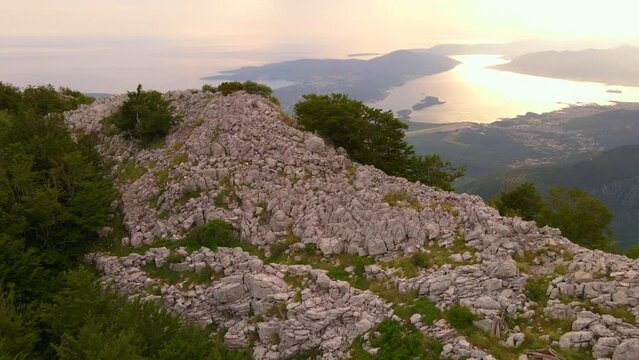 The stunning beauty of the Boka-Kotor bay is captured in this drone footage. The drone glides past a rock, revealing the magnificent panorama of the bay at sunset. This stock video is perfect for any