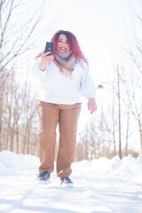 Fototapeta na wymiar Portrait of a smiling plump red-haired woman taking a photo on a smartphone on a walk in winter.