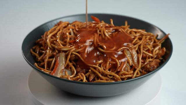 Zeitlupenaufnahme von gebratenen Nudeln, w&auml;hrend chinesische s&uuml;&szlig;-sauer-so&szlig;e dar&uuml;ber gegossen wird