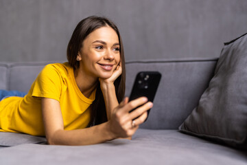 Young woman sit on sofa and use phone happily at home