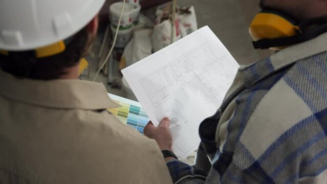 Two architects study the drawing of the apartment, standing in the building. Builders analyze the project documentation, the camera shoots from behind with a view of the drawing. High quality 4k