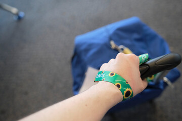 Hand of an unrecognizable person dragging a suitcase, wearing on the wrist a lanyard of sunflowers,...