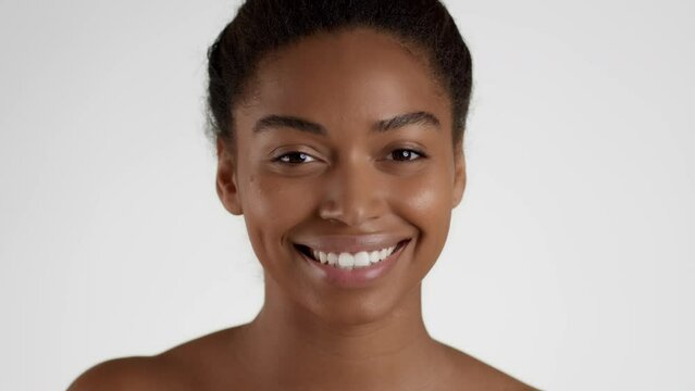 Skin nourishing concept. Young positive african american woman applying serum on face and rubbing it, white background