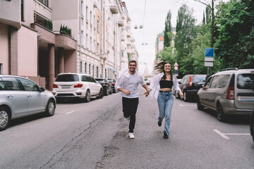 Carefree couple running on city road while holding hands