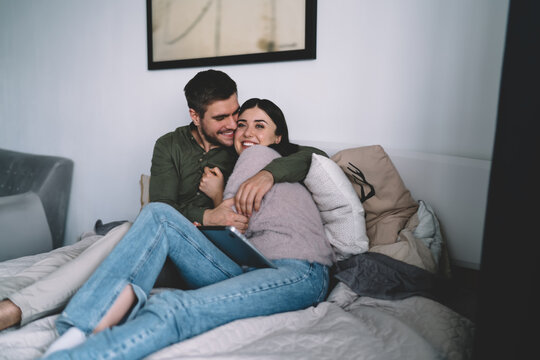 Happy Couple Sitting On Bed Together And Cuddling While Having Laptops