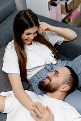 Obraz na płótnie Canvas A loving couple in white t shirts is lying and laughing on the sofa. 