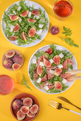 Autumn figs salad with arugula, feta, raw ham in two white plate on yellow background served with...