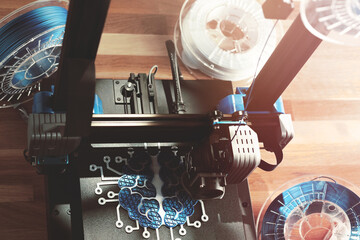 Top view on work space with 3d printer making a symbolic brain sculpture. Wooden desk with filament rolls in warm light. selective focus on print bed and object. Modern intelligent production concept