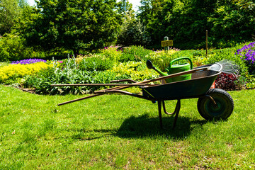 A gardener wheelbarrow with the gardening tools in the gardens. Gardening concept
