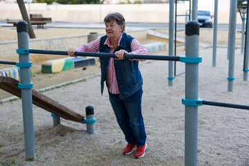 Fototapeta premium An elderly woman is engaged in sports on street simulators, Physical education in retirement