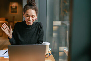 Smiling woman freelance talking with client via video call and discuss project sitting in cafe