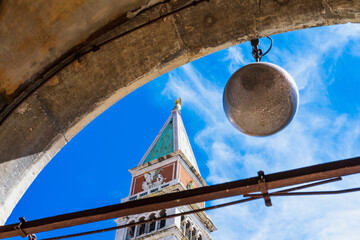 Venetian bell tower of St. Mark's Basilica in Venice against the blue sky from an unusual perspective, the top of the tower with an angel shining in the sun framed by a stone arch, Italian landmarks