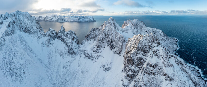 Snow covered mountain range on coastline in winter, Norway. Senja panoramic aerial view landscape nordic snow cold winter norway ocean cloudy sky snowy mountains. Troms county, Fjordgard 