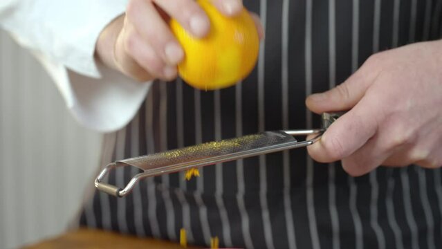 The cook grates the orange peel. Mans Hands Doing Spice From Orange Peel. Slow motion video.
