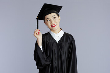 graduate student asian woman holding tassels against gray