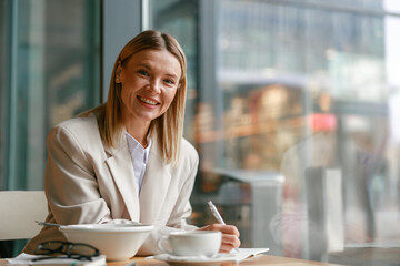 Smiling businesswoman having lunch and making notes while working in cafe