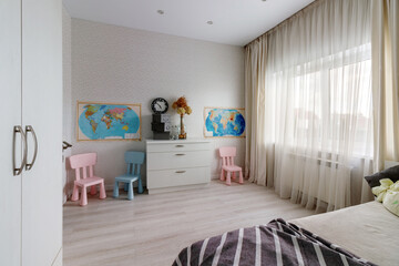 A children's room with a pink and blue chair, a window and a map on the wall