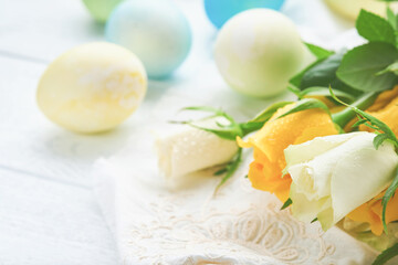 Happy Easter. Easter eggs on rustic table with white and yellow roses. Natural dyed colorful eggs in wooden plate and spring flowers in rustic room.  Toned image. Easter background with copy space.