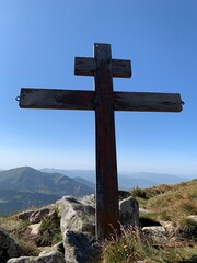 A cross on top of a mountain against a blue sky. A symbol of faith and hope outdoors. Sign of Christianity on a high mountain.
