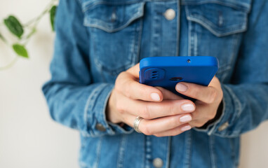 A girl in a denim shirt holds a smartphone in her hands. The concept of working online, freelancing, correspondence, chat. Close-up.