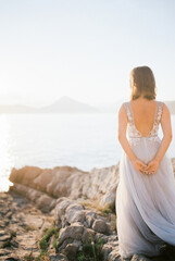 Fototapeta na wymiar Bride stands on a rocky shore and looks at the sea. Back view