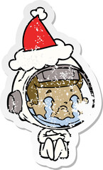 distressed sticker cartoon of a crying astronaut wearing santa hat