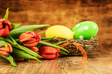 Obraz na płótnie Canvas Two Easter eggs in a nest and tulips on wooden background