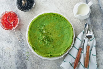 Green pancakes. Round thin green spinach crepe pancakes with red and black caviar and yogurt sauce on gray concrete background. Healthy vegan breakfast. National Pancake Day or Fat Tuesday Day.