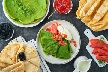 Green and white pancakes assorted. Thin green spinach and white crepe pancakes with red and black caviar, sauce on gray concrete table background breakfast. National Pancake Day or Fat Tuesday Day.