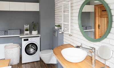 Modern bathroom interior with ceramic wash basin on wooden counter with faucet and round mirror on...