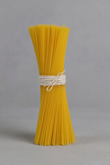 Bunch of spaghetti tied with a rope on a gray background. Gluten free. Spaghetti made of corn and rice flour. Vertical photo